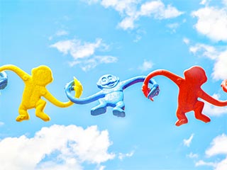 Yellow, blue and red plastic monkeys holding their hands against a blue sky