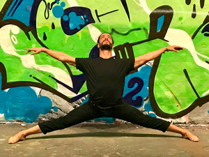 Man doing yoga pose in front of graffiti wall