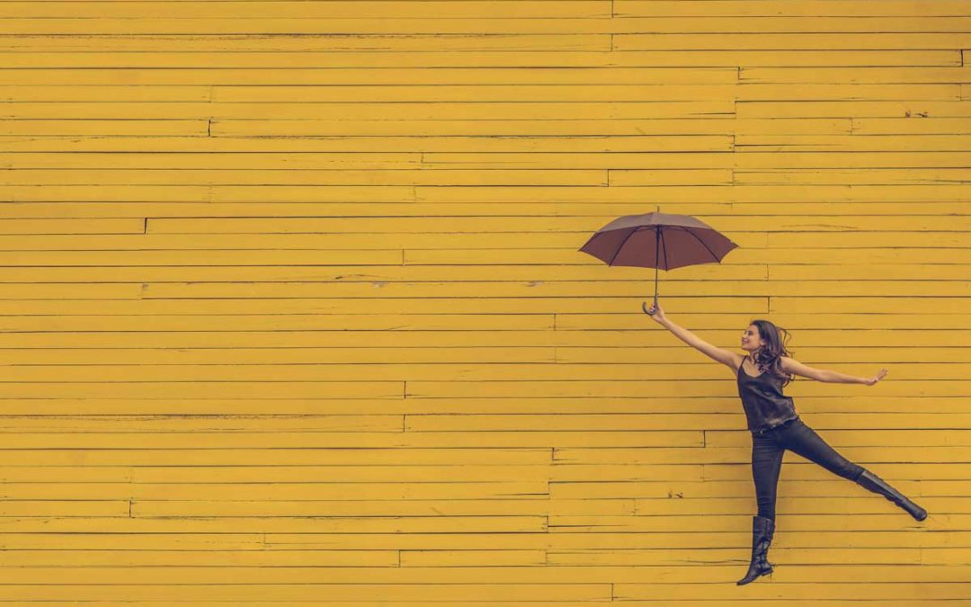 Woman flying with umbrella against yellow background