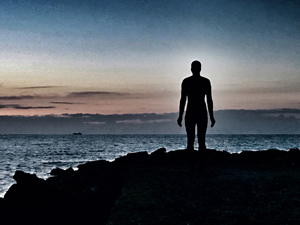 A figure in silhouette standing on rocks looking out to sea