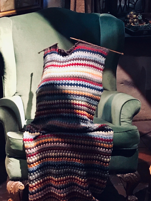 a brightly coloured throw with knitting needles in it on a chair